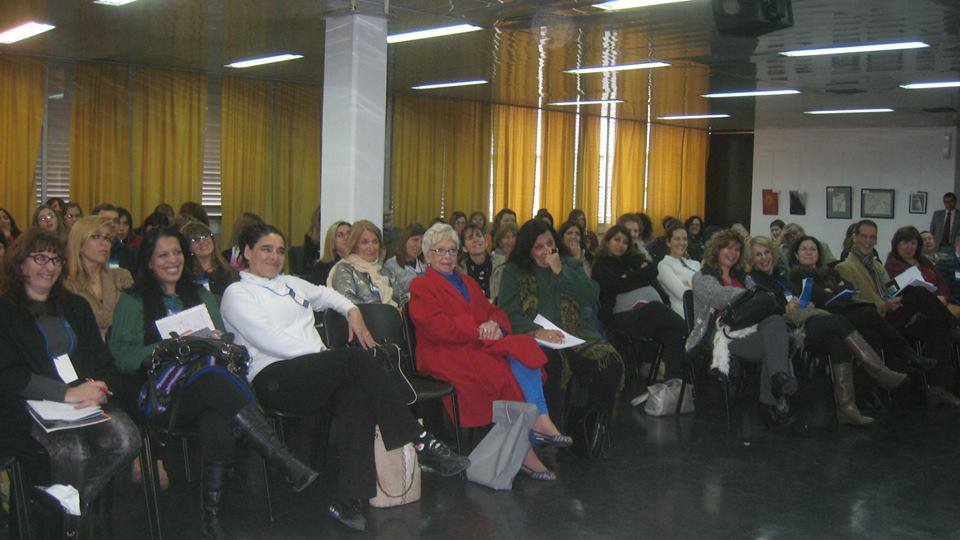 Auditorio colmado de participantes sentados escuchando atentamente y sonriendo